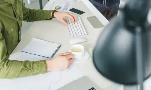 Pracownik biurowy z kawą analizuje wykresy. Czy działalność gospodarczą w domu trzeba zgłaszać?