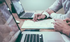 Dwie osoby pracują nad dokumentami przy laptopach. Jedna z nich pisze, co może być związane z ulgą na start zgłoszenie po terminie.