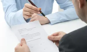 Dwie osoby omawiają umowę. Jedna z nich trzyma długopis, druga dokument, który może dotyczyć PPK a umowa zlecenie.