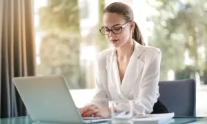 Kobieta w okularach pracuje przy laptopie, przygotowując materiały do działalności nierejestrowanej korepetycje.