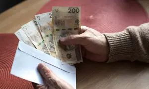 Dłoń trzyma kopertę z banknotami 200 zł. Może to być związane z nowymi zasadami przejścia na emeryturę, tabela z wyliczeniami jest gdzieś obok.