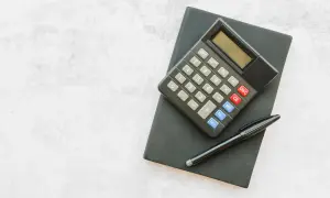 Kalkulator i długopis na czarnym notesie. Zastanawiasz się, ile urlopu przysługuje na 3/4 etatu? Czas to policzyć!
