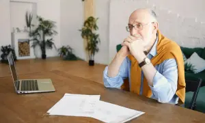 Starszy mężczyzna zamyślony nad dokumentami, być może analizuje chorobowe na wypowiedzeniu.
