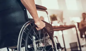 Dłoń na kółku wózka inwalidzkiego. Zastanawiasz się, jaka emerytura po świadczeniu pielęgnacyjnym?