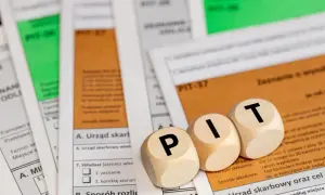 Drewniane klocki z literami "P", "I", "T" leżą na dokumentach podatkowych. Temat: opodatkowanie umowy zlecenia.