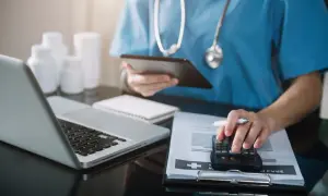 Lekarz analizuje dokumentację medyczną i rachunki, korzystając z kalkulatora i tabletu. Rozliczenia usług medycznych VAT.