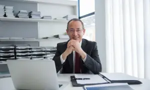 Uśmiechnięty mężczyzna w garniturze siedzi przy biurku z laptopem i dokumentami. Jego mała działalność gospodarcza prosperuje.