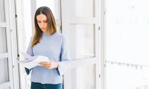 Kobieta w jasnym swetrze analizuje dokumenty, zastanawiając się nad urlopem i wypowiedzeniem.