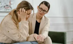 Kobieta w beżowym żakiecie pociesza zapłakaną przyjaciółkę. Czy to siła wyższa, ile płatne wsparcie?