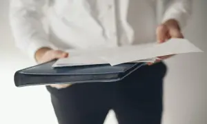 Osoba w białej koszuli trzyma teczkę z dokumentami, symbolizującą rezygnację z funkcji członka zarządu.