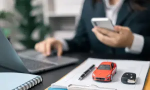 Biznesmen analizuje amortyzację samochodu osobowego 75 czy 100, korzystając z telefonu i laptopa. Na biurku model auta i kluczyki.