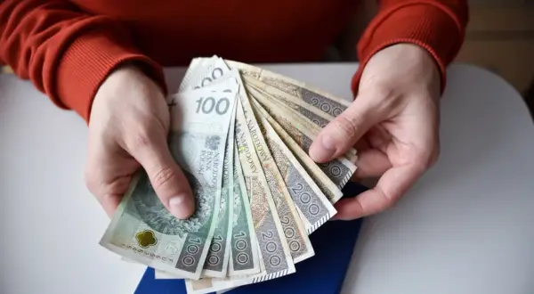 Ręce trzymają polskie banknoty 100 i 200 zł. Zastanawiasz się, ile wynosi renta po świadczeniu rehabilitacyjnym?