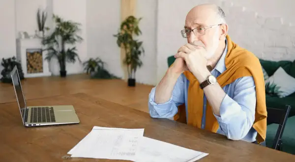 Starszy mężczyzna zamyślony nad dokumentami, być może analizuje chorobowe na wypowiedzeniu.