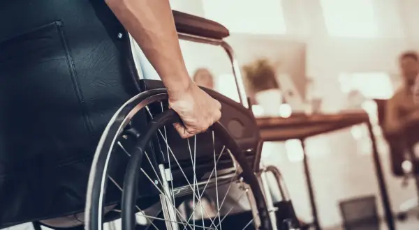 Dłoń na kółku wózka inwalidzkiego. Zastanawiasz się, jaka emerytura po świadczeniu pielęgnacyjnym?