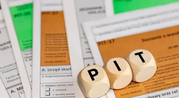 Drewniane klocki z literami "P", "I", "T" leżą na dokumentach podatkowych. Temat: opodatkowanie umowy zlecenia.