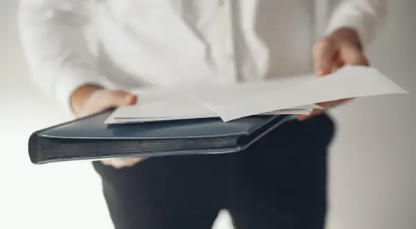 Osoba w białej koszuli trzyma teczkę z dokumentami, symbolizującą rezygnację z funkcji członka zarządu.