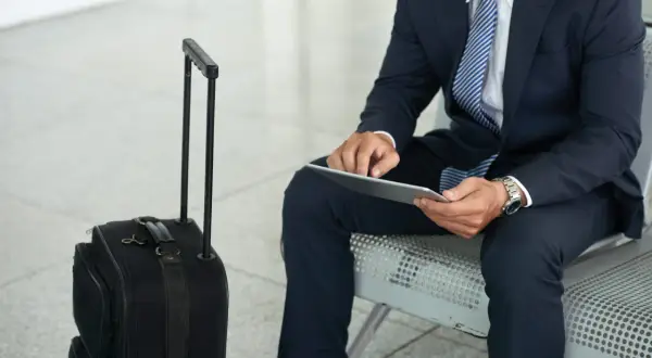Biznesmen w garniturze z walizką czeka na lot. Jego praca poza miejscem zamieszkania wymaga częstych podróży.