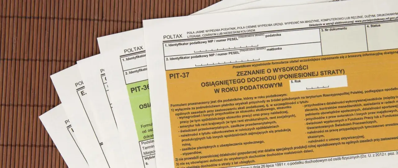Formularze PIT-37 i PIT-36 na drewnianym tle. Dowiedz się, jak zapłacić podatek dochodowy.