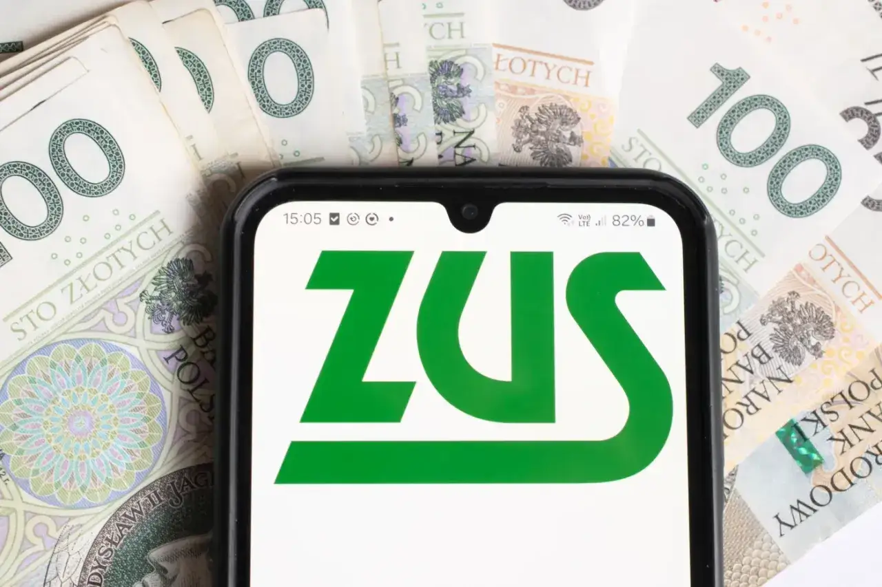 Pierwsza wypłata emerytury z ZUS na koncie. Telefon z logo ZUS na tle banknot&oacute;w 100 zł.