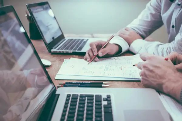 Dwie osoby pracują nad dokumentami przy laptopach. Jedna z nich pisze, co może być związane z ulgą na start zgłoszenie po terminie.