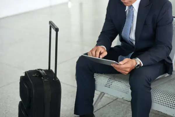 Biznesmen w garniturze z walizką czeka na lot. Jego praca poza miejscem zamieszkania wymaga częstych podróży.
